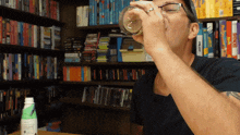 a man drinking from a glass in front of a bookshelf that has a book called ' the maze ' on it