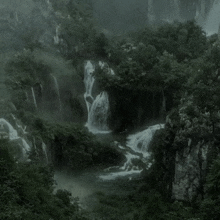 a waterfall surrounded by trees and rocks in a dark forest