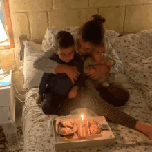 a woman is sitting on a bed with two children and a tray of food with candles on it