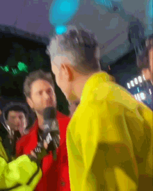 a man in a yellow jacket is talking into a microphone at a party