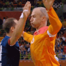 a man in an orange shirt with a medal on his chest is giving a high five to another man