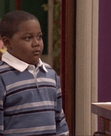 a young boy wearing a blue striped shirt is standing in a room .