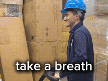 a man wearing a blue hard hat is pushing a pallet truck in a warehouse with the words take a breath above him