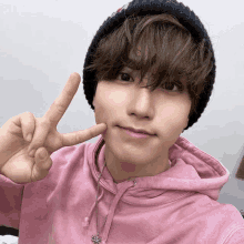 a young man wearing a pink hoodie and a black beanie shows a peace sign