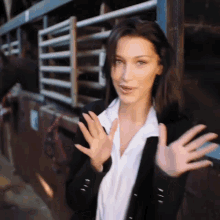 a woman in a black jacket and white shirt is waving her hands in front of a horse stable .