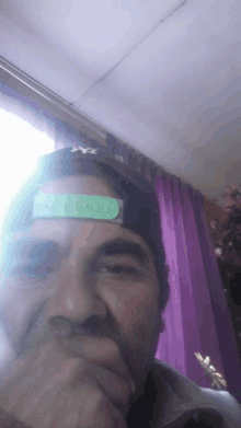 a man wearing a hat has a green sticker on his forehead that says ' x ' on it