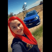 a woman with red hair is taking a selfie with her blue car in the background .