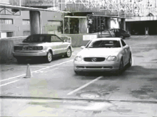 a black and white photo of a car parked in a parking lot with a mercedes logo on the front