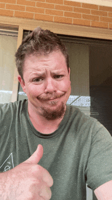 a man giving a thumbs up in front of a brick wall