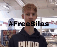 a young man wearing a black puma hoodie stands in front of a sign that says freesilas