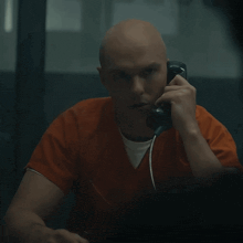 a bald man in an orange shirt is talking on a phone