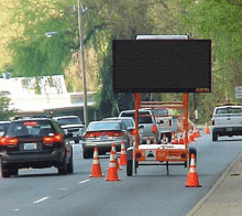 a row of cars are driving down a street with cones and a sign that says ' a ' on it