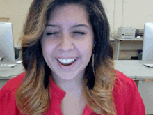 a woman wearing a red shirt and earrings is smiling with her eyes closed