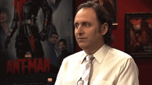 a man in a white shirt and tie stands in front of a movie poster for ant-man