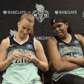 two female basketball players are sitting in front of a banner for barclays
