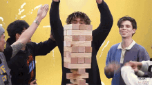 a group of young men are playing jenga and one of them is holding a stack of wooden blocks over his head