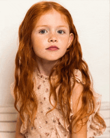 a little girl with long red hair and freckles is wearing a pink dress