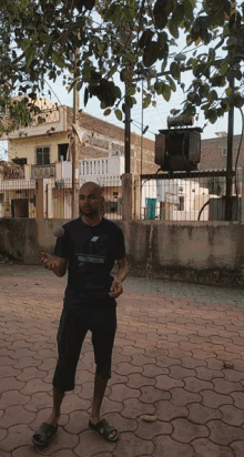 a man wearing a blue shirt that says ' reebok ' on it stands on a brick sidewalk