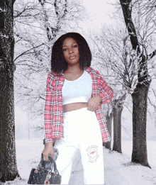 a woman wearing a plaid shirt and white pants stands in the snow