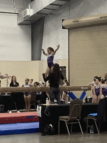 a girl stands on a balance beam in front of a sign that says smyth