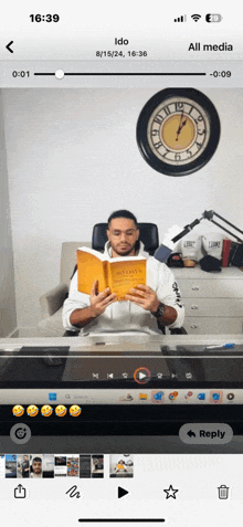 a man is reading a book while sitting in front of a clock on a phone screen