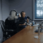 a woman wearing headphones talks into a microphone while a man looks on
