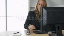 a woman is sitting at a desk in front of a computer screen that says adobe stock on the bottom