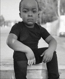 a little boy in a black shirt sits on a ledge