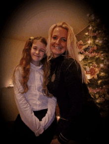 a woman and a little girl are posing for a photo in front of a christmas tree