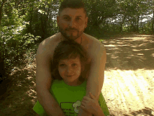 a shirtless man holds a little girl who is wearing a green shirt that says " i 'm a chef " on it