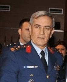 a man in a blue military uniform and tie is standing in a room with other men .