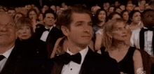 a man in a tuxedo and bow tie is sitting in front of a crowd of people at an awards show .