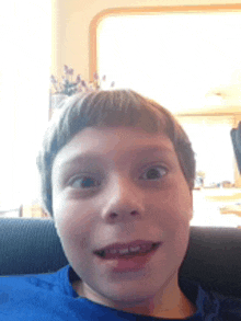 a young boy in a blue shirt is sitting on a couch making a funny face