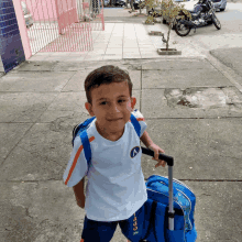 a young boy wearing a white shirt with the letter a on it is pulling a blue suitcase