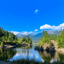 a lake surrounded by trees and mountains with a blue sky