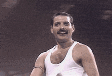 a man with a mustache is wearing a white tank top and smiling while holding a microphone .