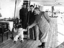 a man in a suit is standing next to a little boy sitting on a wooden swing .