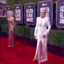 a woman in a white dress stands on a red carpet in front of a wall with signs that say golden globe awards