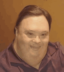 a man with down syndrome is smiling for the camera while wearing a purple shirt and tie .