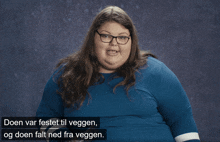 a woman wearing glasses and a blue shirt says " doen var festet til vegen og doen falt ned fra vegen "