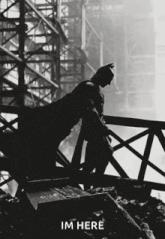 a silhouette of batman leaning on a railing with the words im here written below him