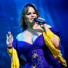 a woman in a purple dress and yellow scarf is singing into a microphone on a stage .