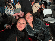 two women are posing for a selfie in a crowded room