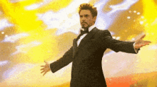 a man in a tuxedo is standing with his arms outstretched in front of a yellow background .