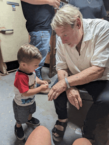 a little boy in a red white and blue shirt is standing next to an older man in a white shirt