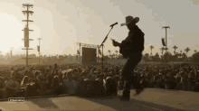 a man in a cowboy hat is playing a guitar in front of a crowd at a music festival .