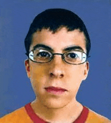 a young man wearing glasses and a red shirt is looking at the camera with a blue background .