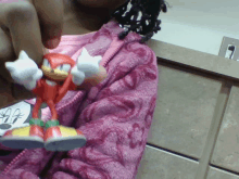 a girl in a pink jacket is holding a sonic the hedgehog figure