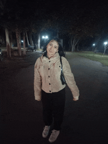 a woman standing in a park at night wearing a white jacket