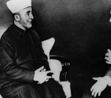 a man in a white hat sits in a chair with another man